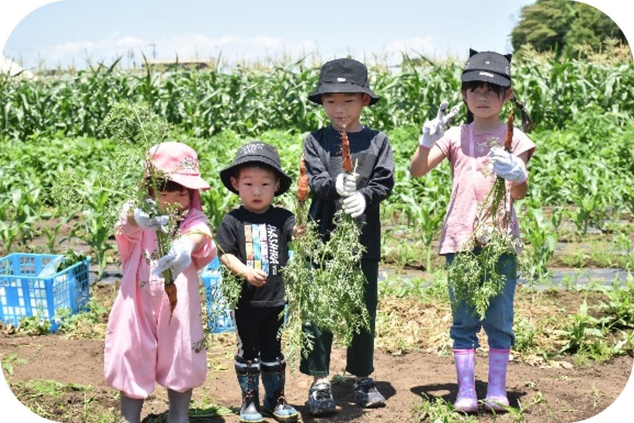 子ども4人が収穫した野菜を持ってポーズをとっている