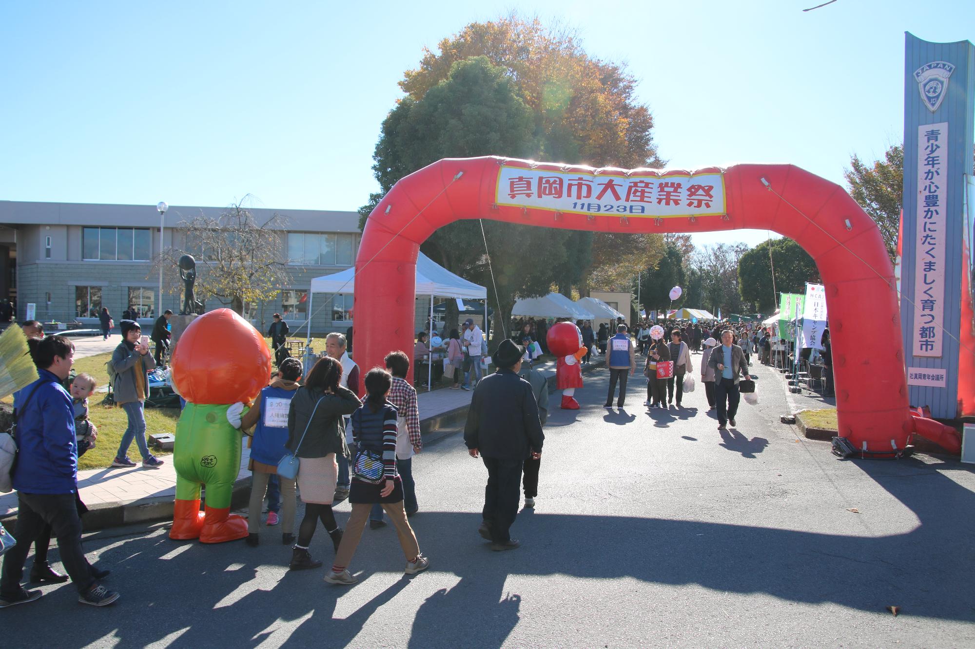 「真岡市大産業祭」と書かれたアーチの近くでマスコットキャラクターたちが来場した人たちを歓迎している写真