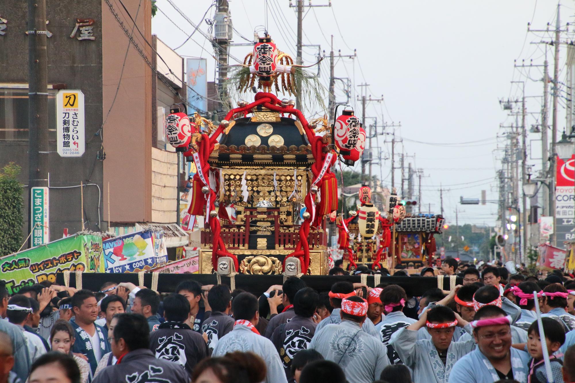 提灯のついた大きな神輿が鉢巻きを付けた人たちによって運ばれている写真