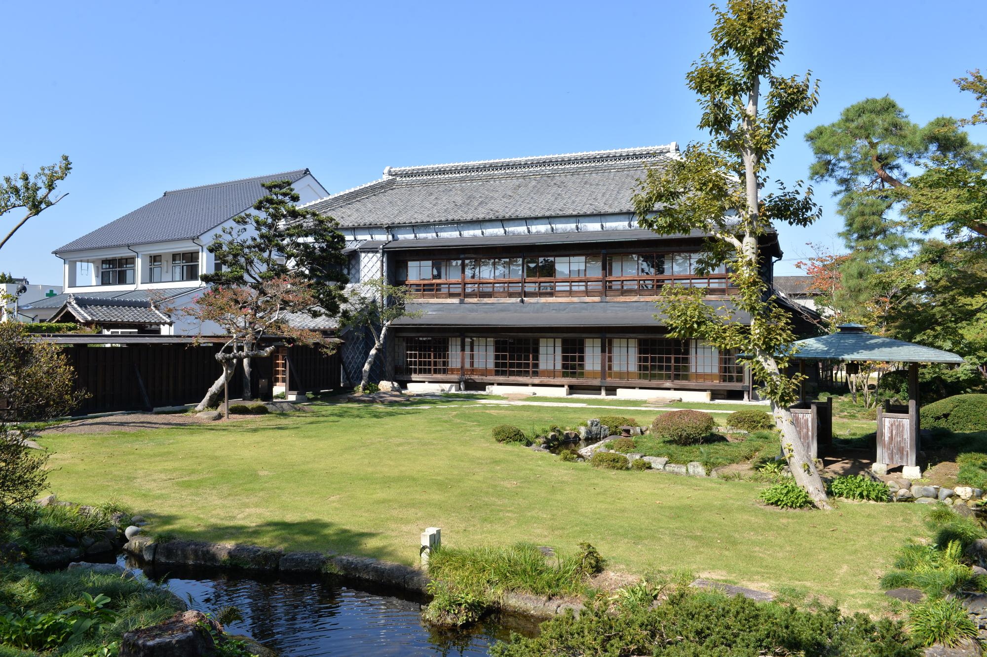 日本庭園の奥に建つ大きな和風の2階建ての建物全体を写した写真