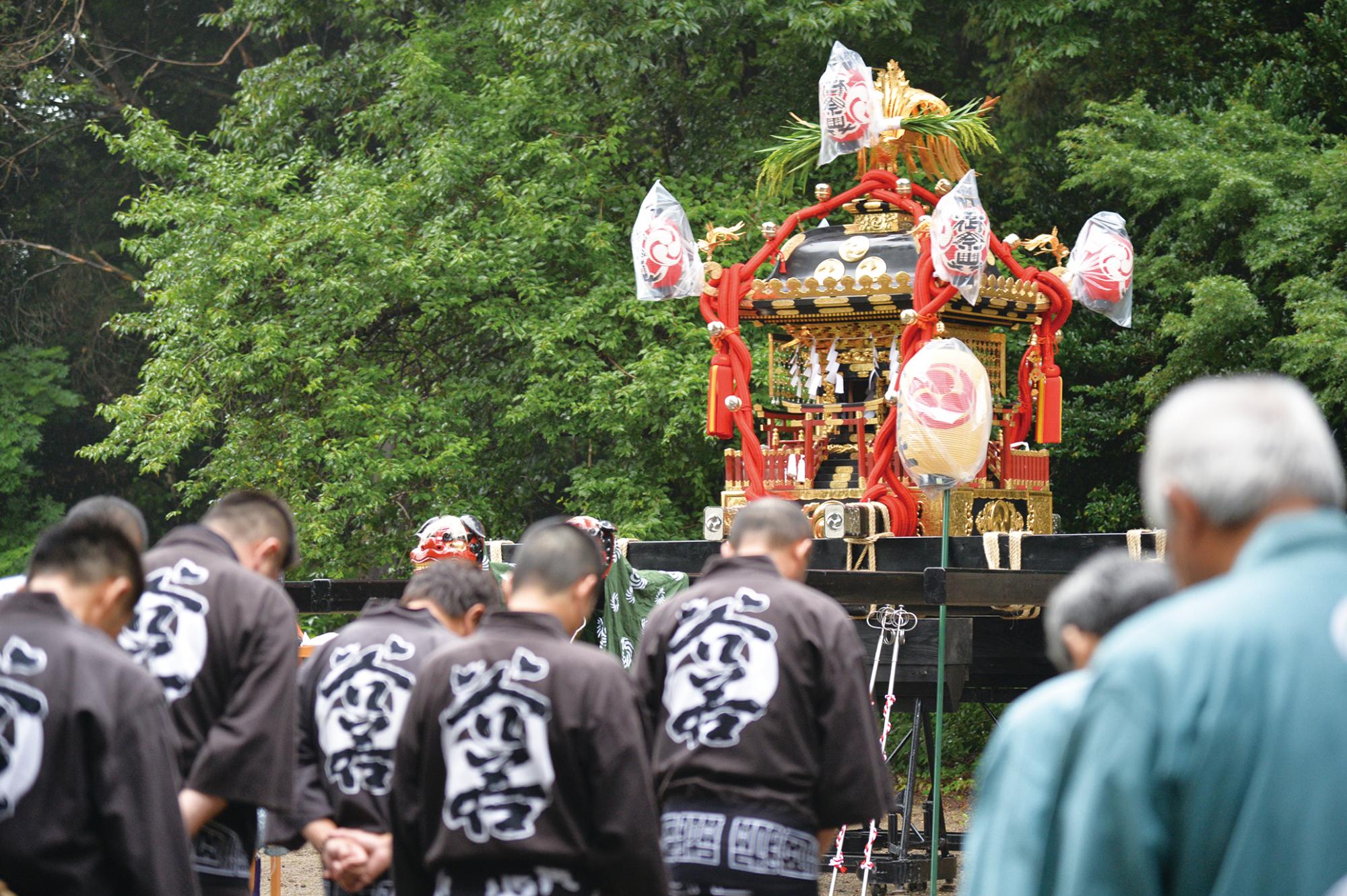 お神輿の前で法被を着たたくさんの人達が頭を下げている写真