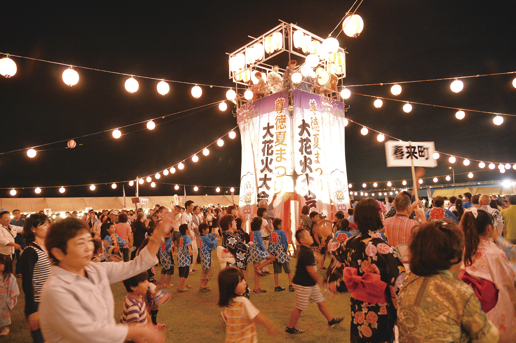 中央に「尊徳夏まつり 大花火大会」と書かれライトアップされた小さな舞台の周りでたくさんの人達が踊っているお祭りの写真