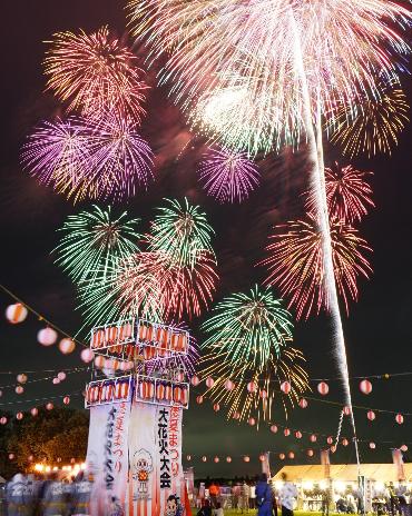 櫓の奥で打ち上げられた様々な色の花火の写真