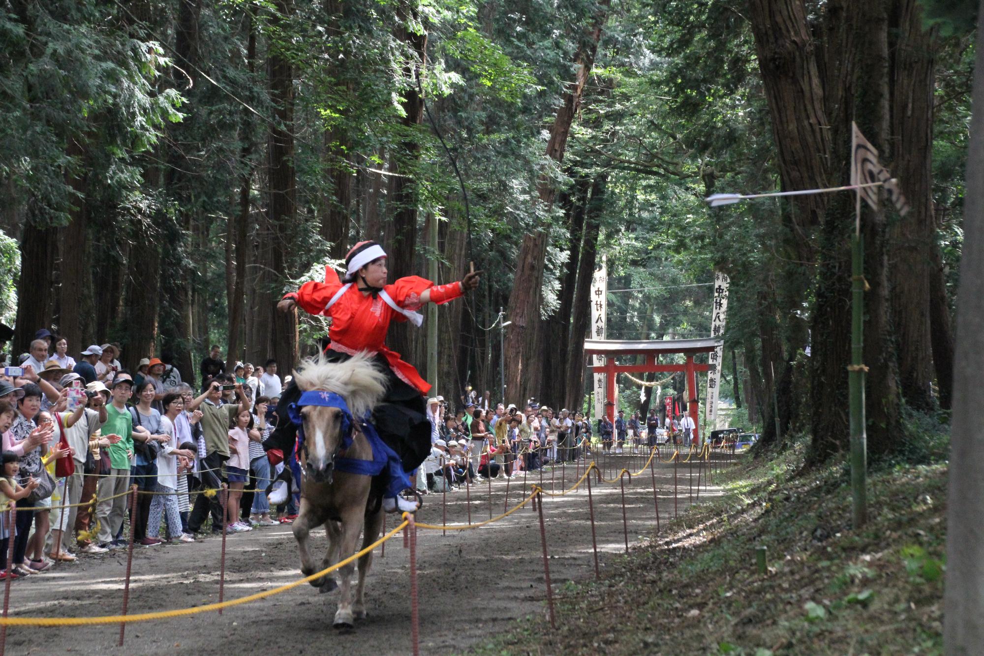 赤い着物を着た人が流鏑馬で矢を射った瞬間の写真