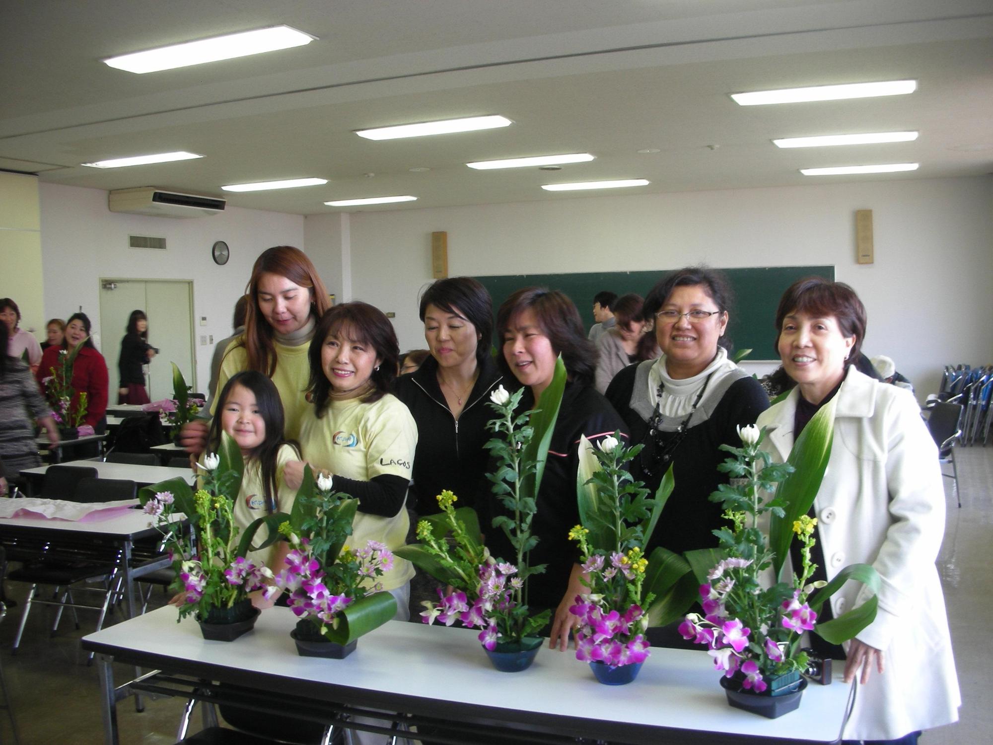 生け花の前で微笑む7人の女性の写真