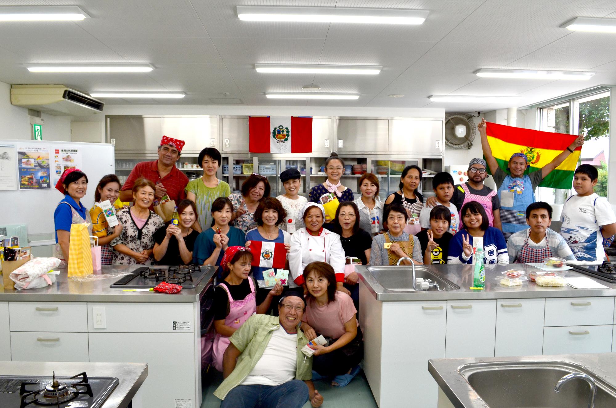 ペルーやボリビアの国旗がある調理室で参加者達が集まって記念撮影をしている写真