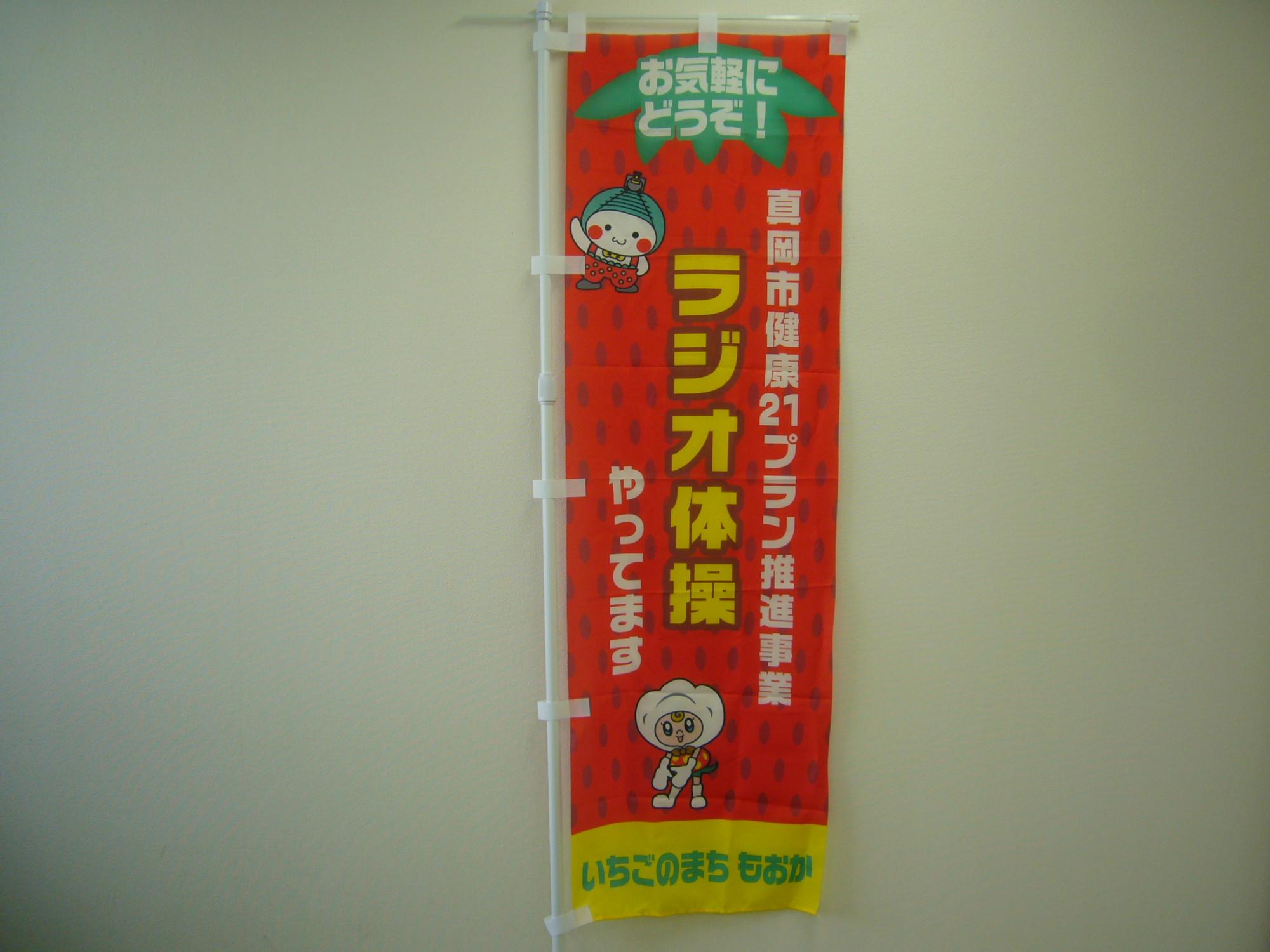 「真岡市健康21プラン推進事業 ラジオ体操 やってます」と書かれた赤いいちご模様ののぼり旗の写真