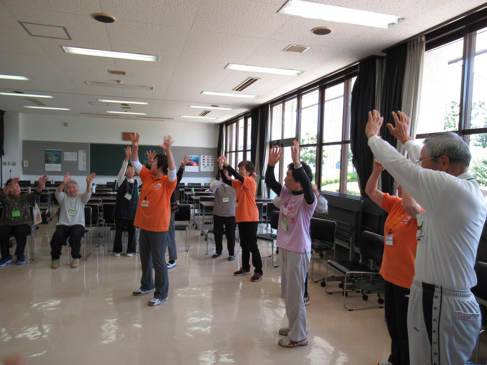 椅子に座っている参加者、立っている参加者の方々が両手を上に挙げて体操をしている大内たんぽぽ会の体操の様子の写真