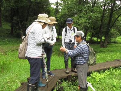 大人たちが集まって、指導員が持っている生き物を観察している写真です。