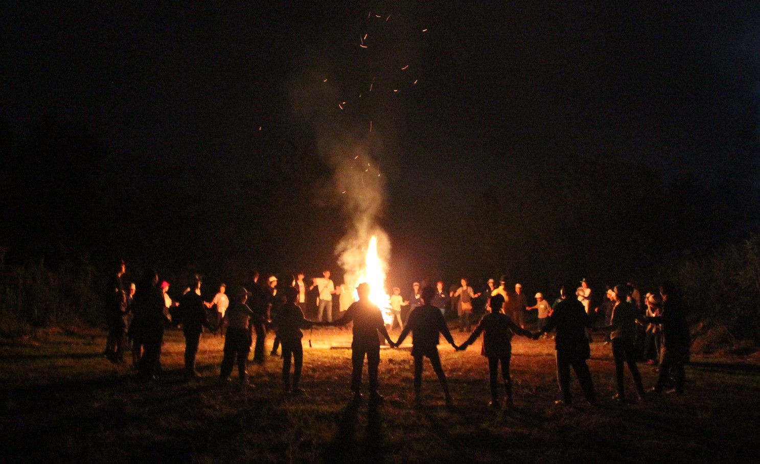 参加者が、焚き火を囲んで大きな輪を作り、キャンプファイアーをしているの様子の写真