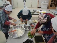 巻きずしを作るために、巻きすの上に、焼き海苔や酢飯、具材を置いている女性たちの写真