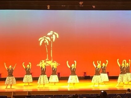 舞台上でお揃いのフラダンス衣装を着て踊りを踊っている写真
