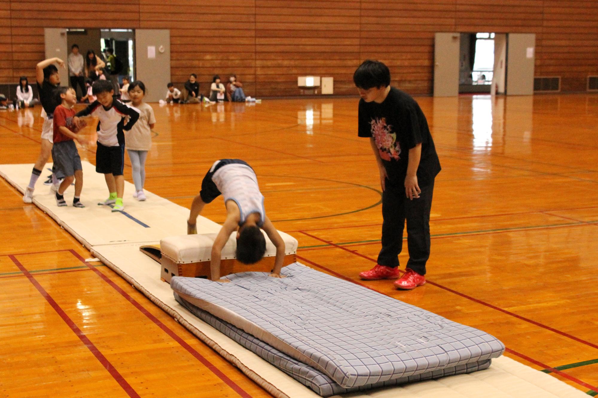 跳び箱を飛び越えて前回りをするこどもと見守る講師
