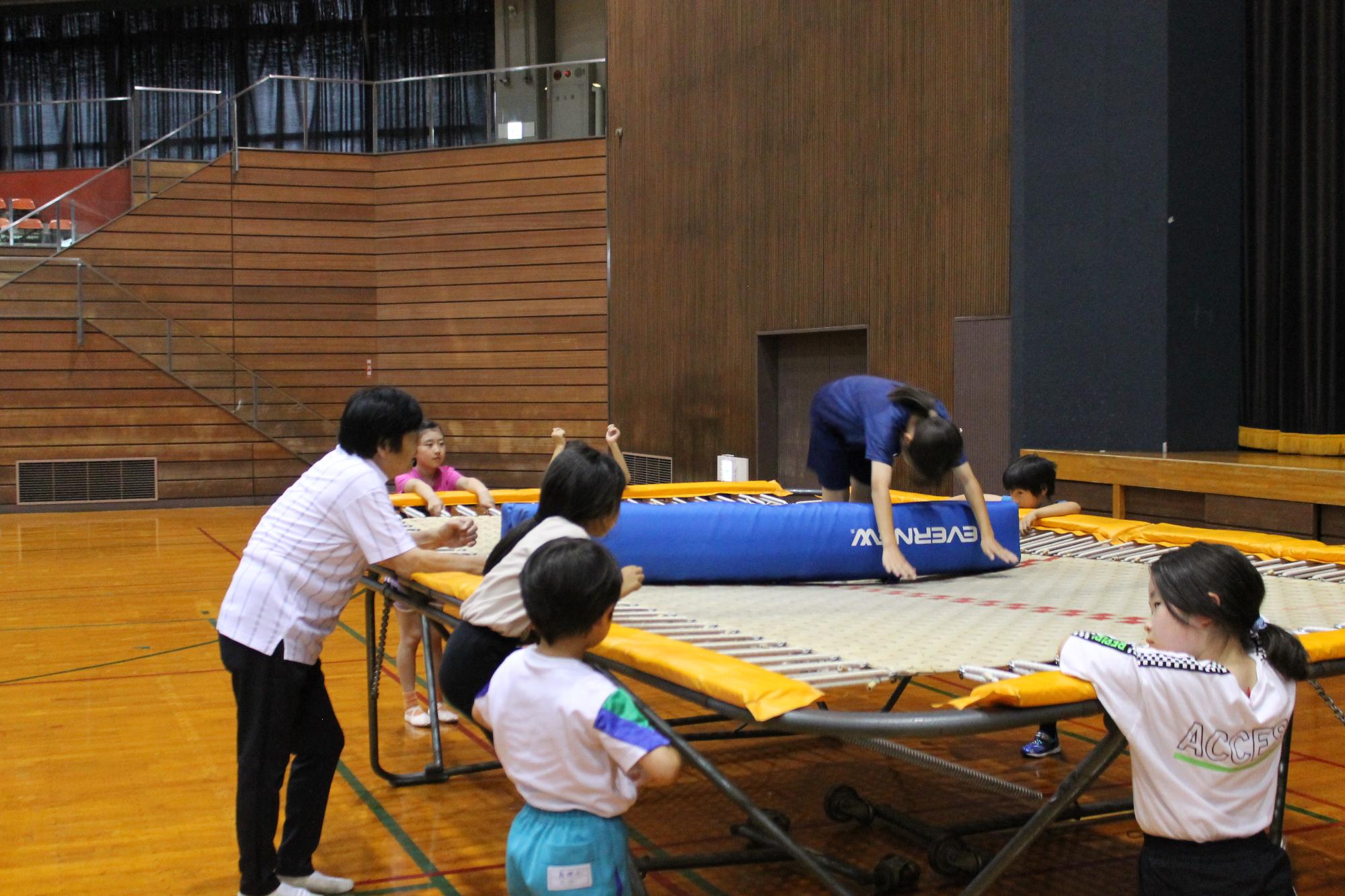 トランポリンの上に置かれた障害物の上を上手に飛ぶこども