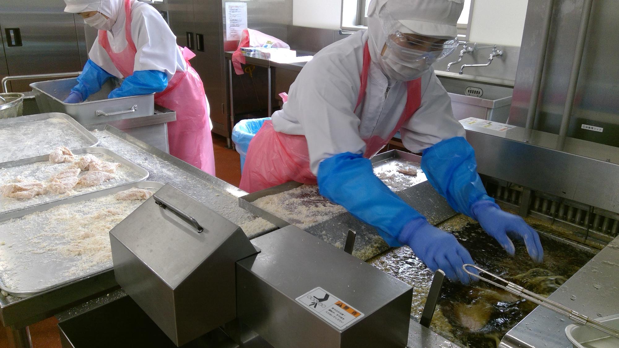 調理員が鶏肉をフライヤーの油の中に入れている写真