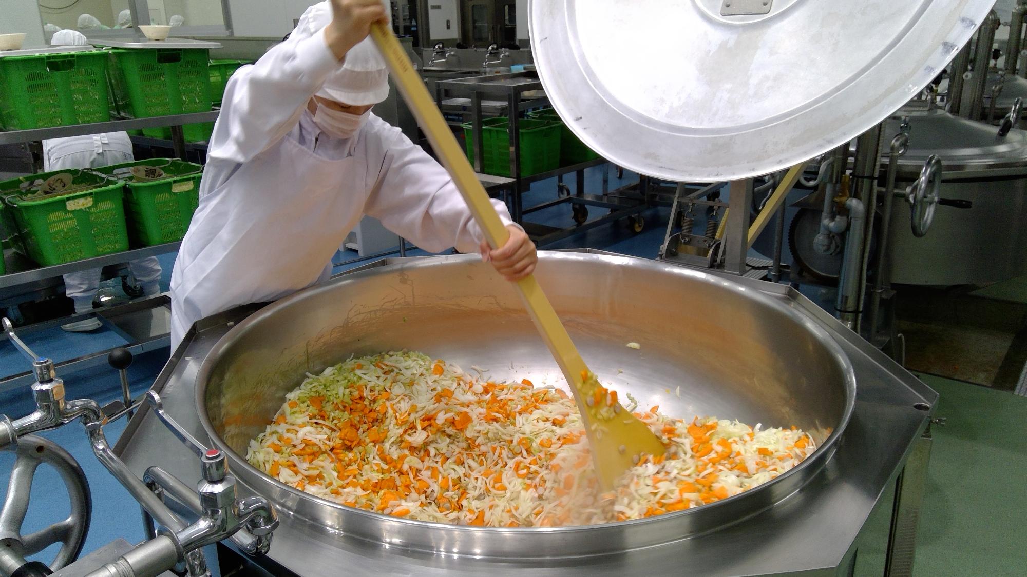 調理員が大きなヘラを使い汁物を作っている写真