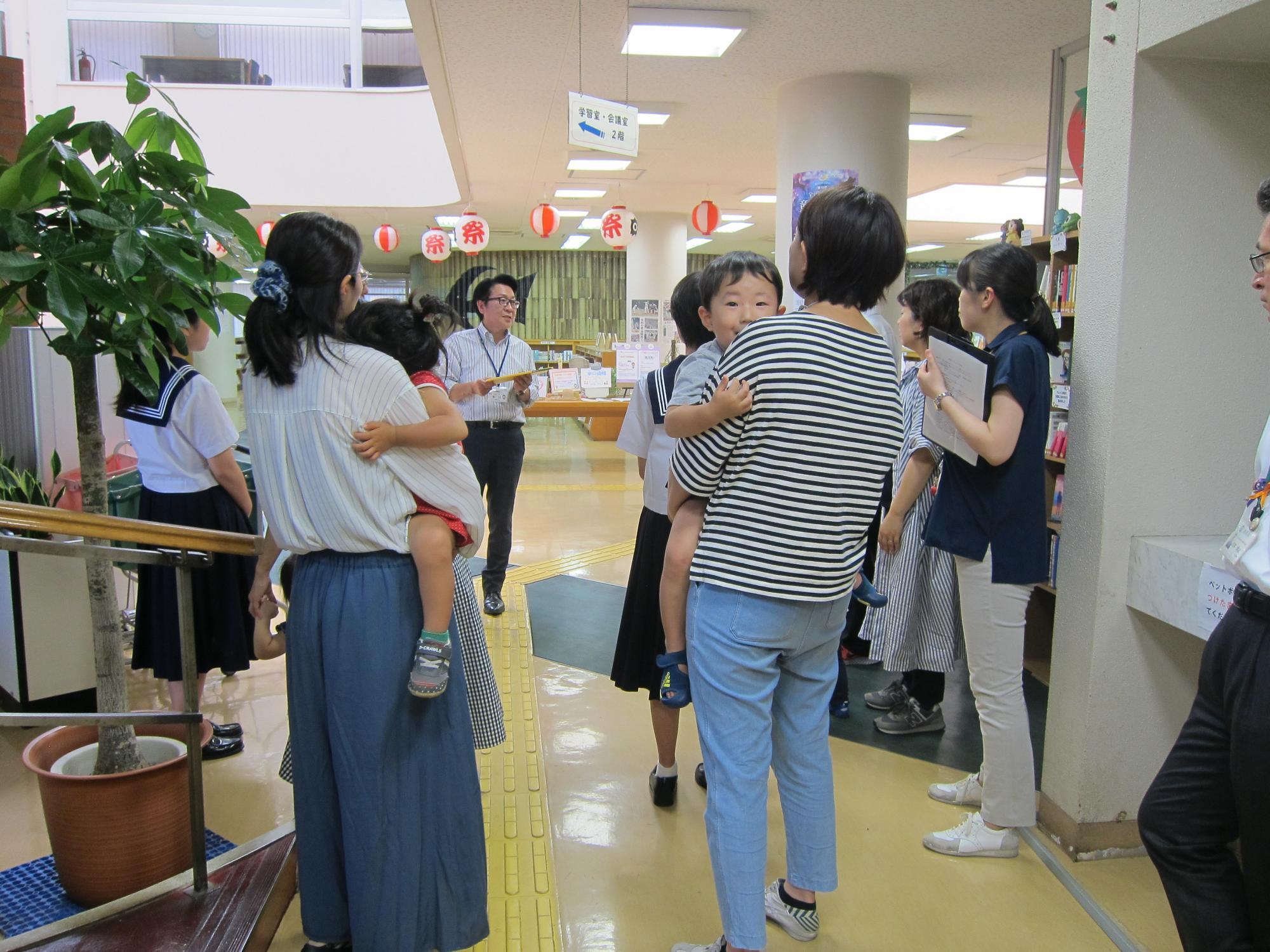 制服を着た学生や、子供を抱っこしているお母さんたちが図書館見学に参加している写真