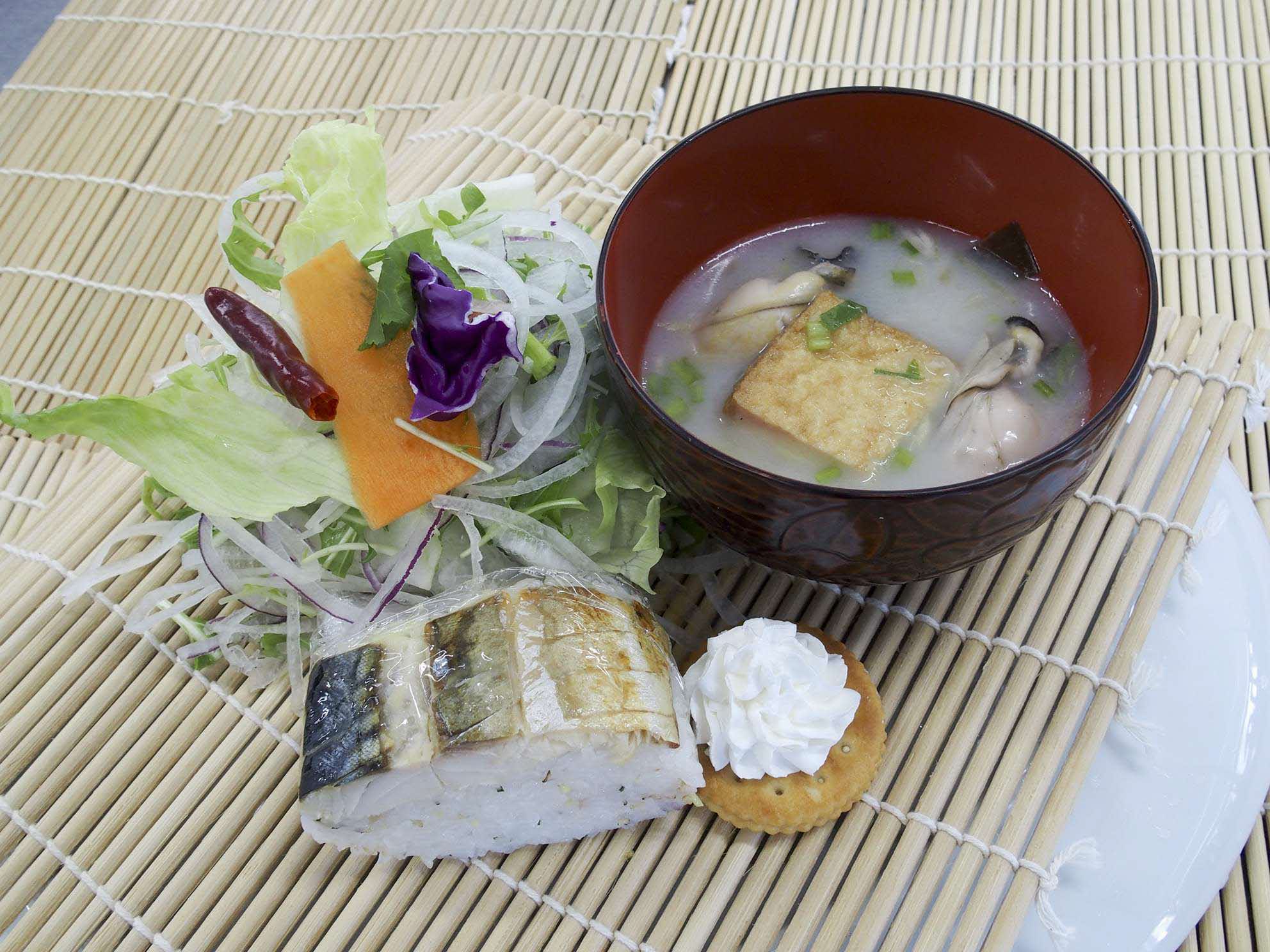 巻きすの上に盛り付けられた焼鯖寿司、サラダ、味噌汁の写真