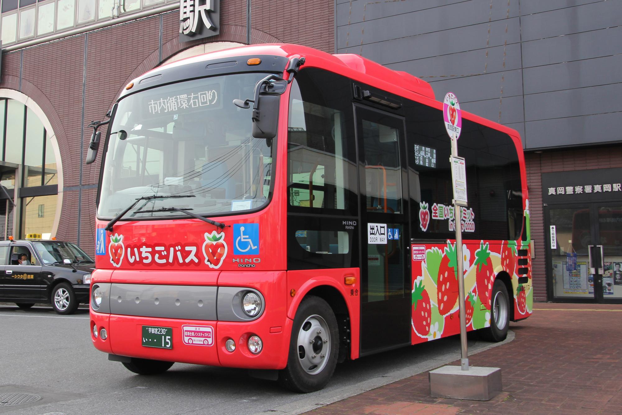 バス停前に停車している全体が赤く、車体に苺の絵が描かれているいちごバスの写真