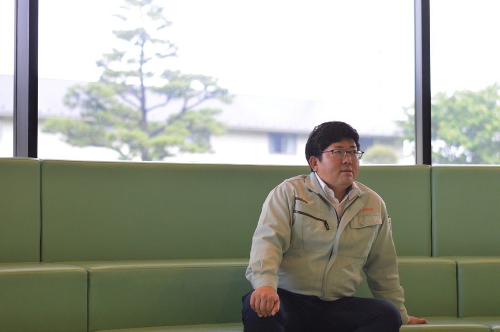 緑色のソファーに腰かけ遠くを見ている上澤 宏行さんの写真