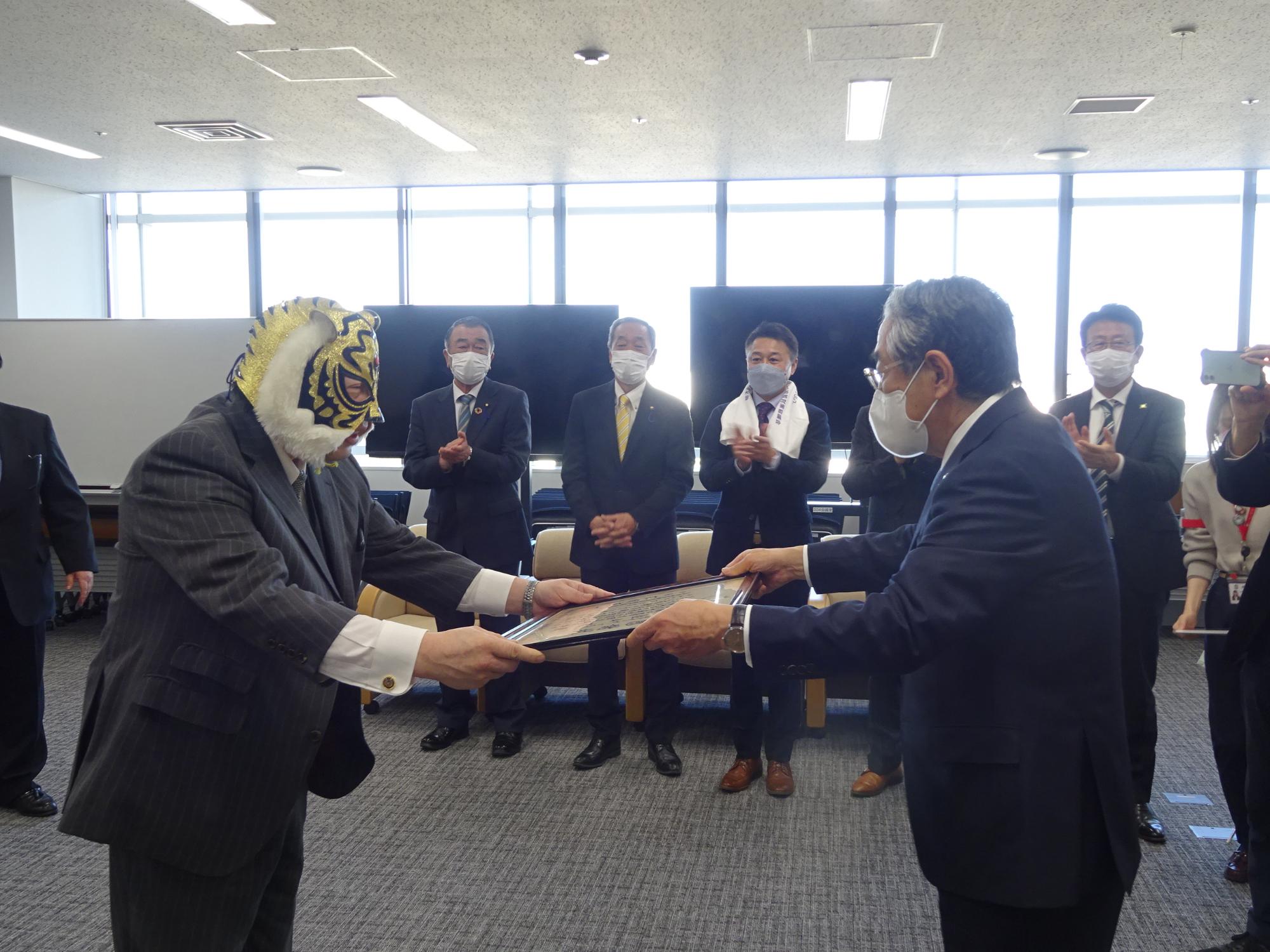 市長から感謝状を受け取っているタイガーマスクを被った佐山聡さんの写真